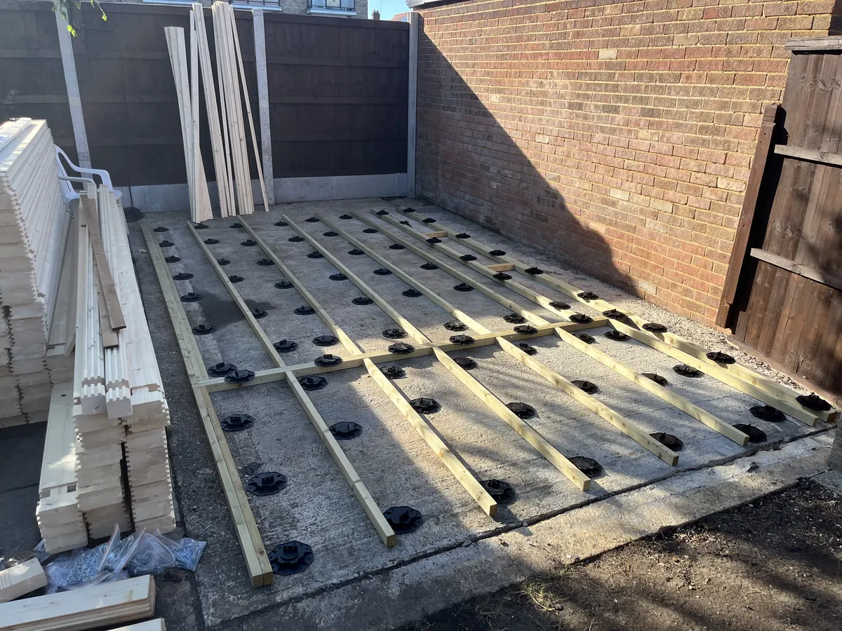 Rows of treated joists sitting on dozens of black adjustable plastic feet on the old concrete slab