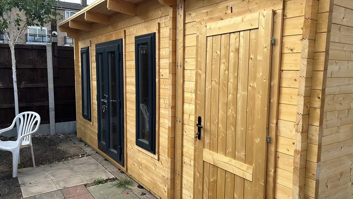 The front of the cabin in bare timber with the dark grey uPVC double doors, windows and the side store door fitted