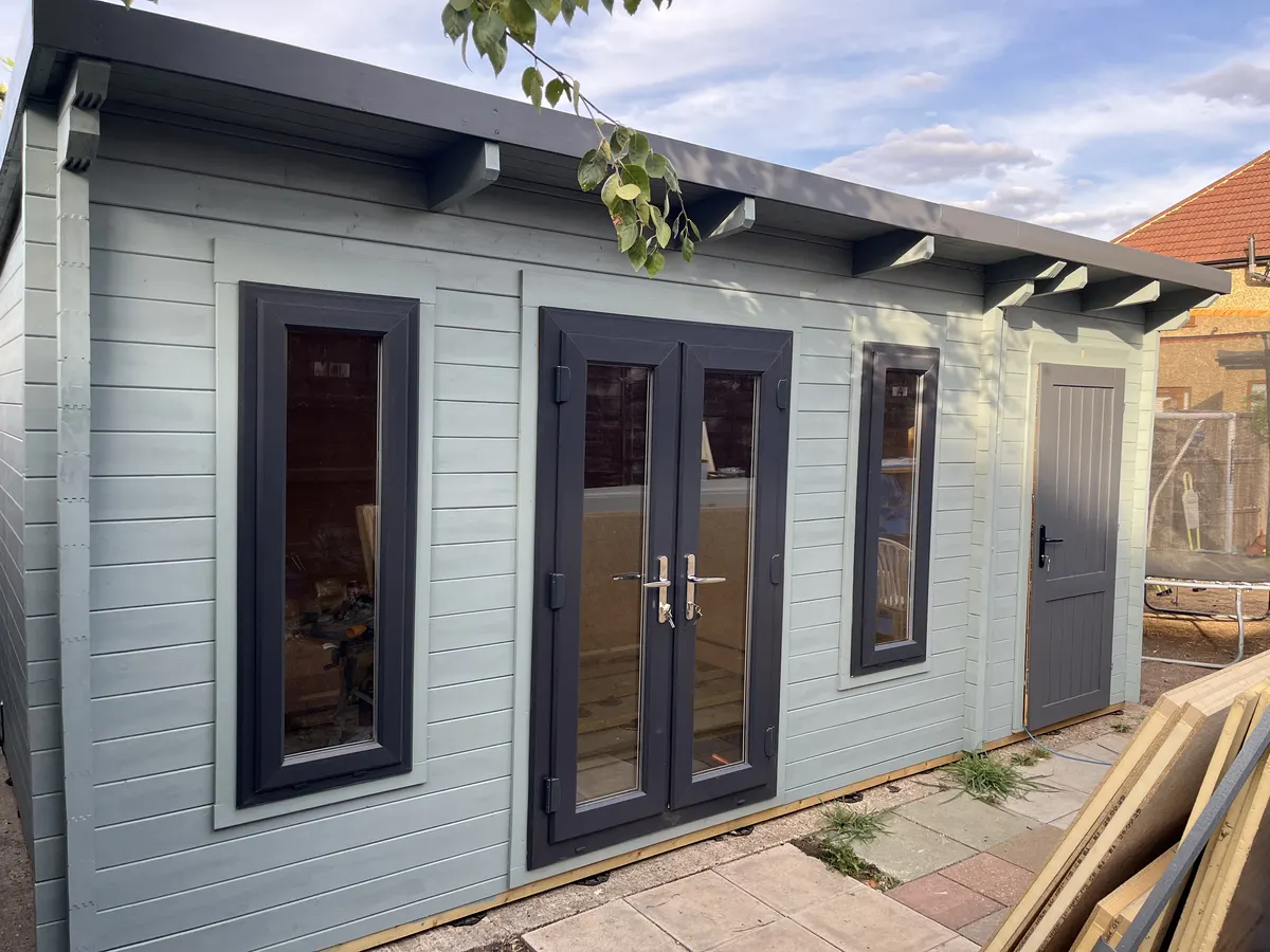 The finished cabin painted pale blue grey, with charcoal uPVC double doors and windows and a charcoal side store door